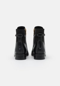 Bottes noires en cuir à tige cheville avec panneaux latéraux élastiques, fermetures éclair dorées et détails de logo au talon. Texture lisse, talon bloc robuste.