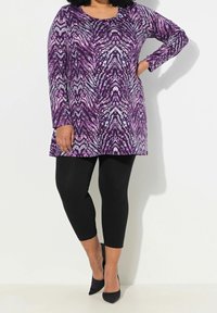 Tunique à manches longues dans un motif abstrait violet et gris, associée à des leggings noirs et des escarpins noirs pointus. Tissu lisse et extensible.