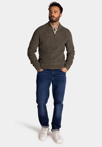 Grijze gebreide trui met een ritssluitingkraag, gecombineerd met blauwe spijkerbroeken en witte sneakers, met een gestructureerde stof en een casual pasvorm.