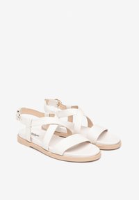 Sandali bianchi in pelle con fascia incrociata, tacco aperto e suola piatta marrone chiaro. Fibbia sulla cinghia alla caviglia.