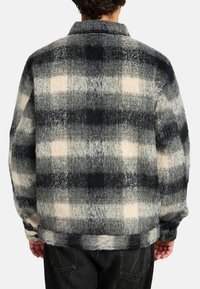 Kariertes Fleece-Hemdenjacke in Schwarz, Grau und Cremefarben. Verfügt über einen Kragen, lange Ärmel und eine lockere Passform mit weicher Textur.