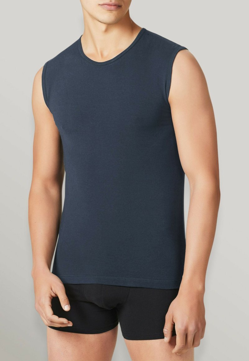 Camicetta senza maniche di cotone color navy con scollatura rotonda, forma aderente e texture liscia, abbinata a biancheria intima nera attillata.