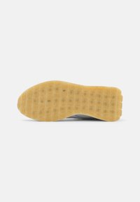 Semelle de chaussure avec une bande de roulement en caoutchouc brun clair présentant un motif en forme de grille et une légère texture sur fond blanc.