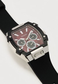 Montre Square Guess avec un cadran texturé bordeaux, trois sous-cadrans, bracelet en caoutchouc noir et accents en acier inoxydable.