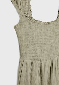 Robe vert clair texturée avec un corsage smocké, des bretelles volantées et une jupe fluide. Conçue en tissu léger et doux.