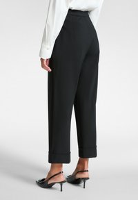 Pantaloni neri a vita alta con una vestibilità ampia, dotati di risvolti. Il tessuto è morbido, abbinato a scarpe con tacco aperte nere.