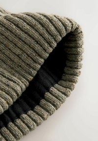 Dzianinowa czapka w odcieniu szaro-zielonym z prążkowaną fakturą, z miękką czarną podszewką. Krawędź ma podwinięty ściągacz dla dodatkowego ciepła i stylu.