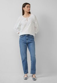 Biała bawełniana bluzka z detalami w stylu eyelet, długimi puff sleeves, okrągłym dekoltem i wycięciem w kształcie łezki na środku. Połączona z jasnoniebieskimi prostymi dżinsami.