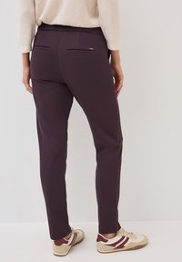 Pantalons de yoga violets avec une taille élastique, dotés de deux poches zippées à l'arrière et de jambes fuselées, associés à des baskets multicolores.