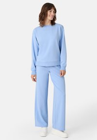 Sudadera azul claro con cuello redondo y dobladillo acanalado, combinada con pantalones de pierna ancha a juego. La tela parece suave y lisa.