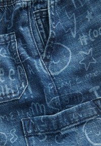 Sinine denimpind, millel on heledatest toonidest käsitsi kirjutatud mustrid ja kujundid. Omab esipockets ja tekstureeritud pinda.