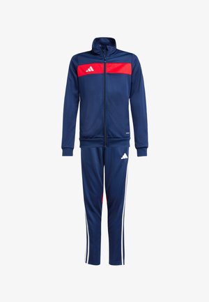 Mørkeblå træningsdragt med et rødt panel på den øverste del af brystet. Har hvide striber på bukserne og et Adidas-logo på både overdel og underdel.