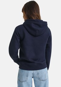 Navyblauwe hoodie met een trekkoordcapuchon, zachte textuur en lange mouwen, gecombineerd met lichtblauwe denim jeans. Eenvoudig en casual ontwerp.