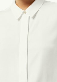 Camicia bianca con colletto, caratterizzata da una chiusura a bottone, tessuto di cotone morbido e un design pulito senza motivi o accenti visibili.