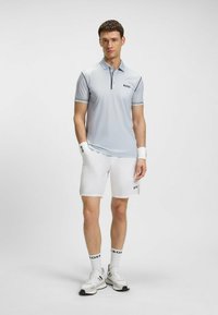 Polo shirt azzurro chiaro con logo, pantaloni corti bianchi, calze bianche e scarpe sportive. Presenta strisce a contrasto sulle maniche e design del colletto classico.