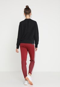 Sudadera negra con dobladillo redondeado y puños de canalé, combinada con leggings burdeos que tienen rayas blancas y detalles texturizados en las piernas.