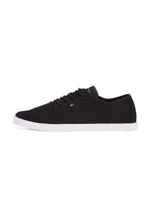 Czarny nisko osadzony sneaker z białą gumową podeszwą, czarnymi sznurowadłami oraz małym czerwono-biało-niebieskim detalem w kształcie flagi po boku.