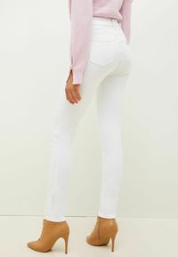 Jeans blancos ajustados con cintura alta y bolsillos traseros, combinados con botines de tacón alto beige. El look se completa con un suéter de color rosa claro.