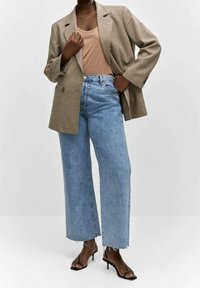 Blazer oversized marrón a cuadros, top beige sin mangas, vaqueros de pierna ancha azul claro con dobladillo deshilachado y sandalias negras de tacón.