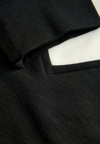 Zwarte stof met ribbelstructuur, voorzien van een gevouwen rand die een gladde witte voering en een zwart rechthoekig accent onthult.