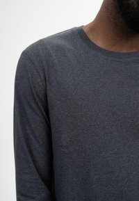 Graues Langarmshirt mit Rundhalsausschnitt, aus weichem Stoff gefertigt, mit glatter Textur und einfacher Konstruktion, minimaler Detailverarbeitung.