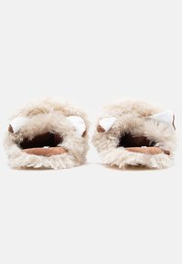 Minkasti krēmkrāsas čības ar noapaļotu dizainu, baltiem ausu akcentiem un mīkstu brūnu iekšpusi. Raupja ārējā auduma struktūra nodrošina siltumu un komfortu.