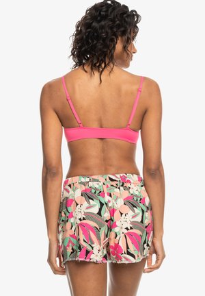 Top bralette rosa con tirantes ajustables, combinado con pantalones cortos de patrón floral colorido que presentan una mezcla de rosa, verde y negro.