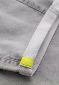Tejido gris con una superficie texturizada; presenta un acento amarillo en el borde. El diseño incluye un dobladillo bien doblado.