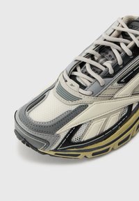 Sapatilha atlética leve com parte superior em malha e sintético nas cores creme, cinza e preto. Detalhes texturizados e uma sola com amortecimento garantem conforto.