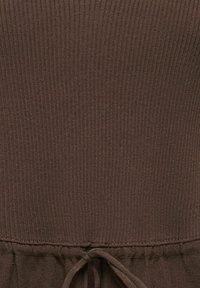Gros plan d'un tissu tricoté côtelé marron avec une couture froncée et un cordon noué en bas au centre.