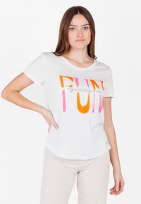 T-shirt bianca in cotone con scollatura rotonda, decorata con grande testo multicolore: "DIVERTIMENTO" in arancione e rosa, e la frase sottostante in grigio.