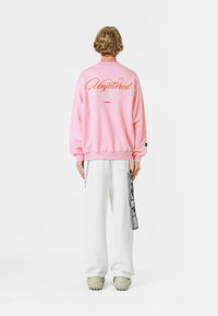 Sudadera rosa con el texto "Sin restricciones" en la parte posterior, combinada con pantalones anchos blancos y calzado beige con suelas texturizadas.