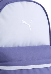Vijolična nahrbtnik s sivo zgornjo sekcijo, ki ima belo Puma logo. Teksturovana tkanina in kontrastna bela črta.