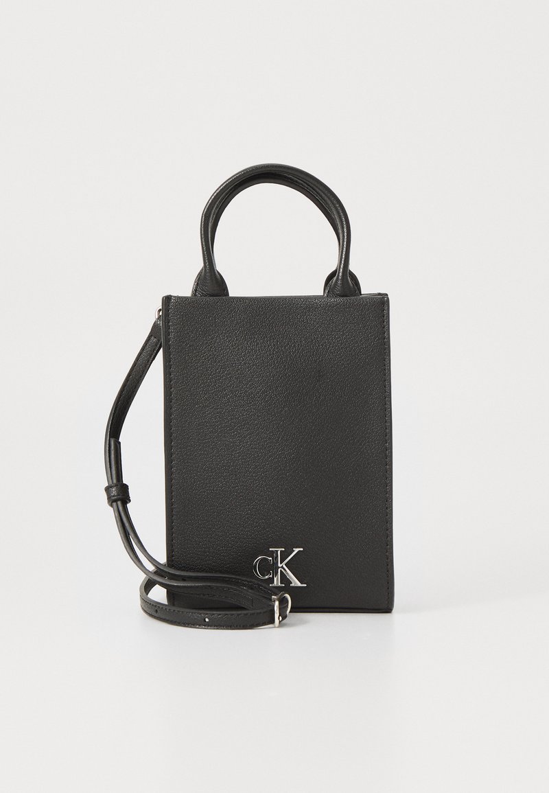 Bolso de mano de cuero negro con un diseño minimalista. Presenta asas superiores, una correa de hombro desmontable y un acento de logo en plata.