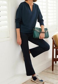 Sweat-shirt marine à col en V, associé à un pantalon évasé marine. Un sac à main vert avec une bandoulière chaîne et des baskets bicolores à lacets.