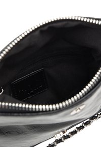 Interno di una borsa a tracolla in pelle nera con una tasca con zip e una fodera in tessuto morbido. Presenta chiusura con zip in argento e un'etichetta rettangolare.