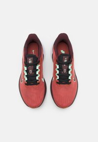Scarpe sportive rosse e nere con tomaia testurizzata, lacci neri, accenti turchesi e una suola intermedia bianca. Logo Nike sui lati.