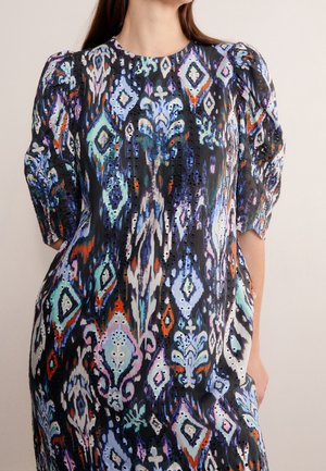 Frau trägt ein mehrfarbiges Kleid mit Muster, Puffärmeln und Lochstickerei auf schwarzem Stoff.