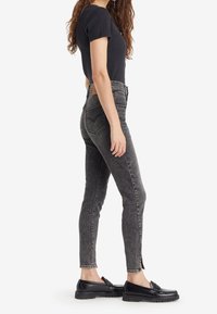 Jeans negros de corte alto y ajustado con textura deslavada, que cuentan con un corte en el tobillo. Combinados con una blusa negra ajustada y mocasines negros.