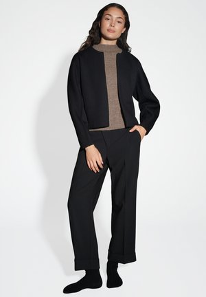 Schwarze cropped Jacke über einem braunen gerippten Pullover, kombiniert mit schwarzen weiten Hosen. Glatte Stofftextur, minimalistisches Design und klare Linien.