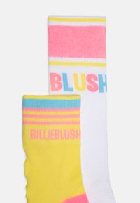 Calcetines con colores alternos: amarillos con rayas rosas y azules, y blancos con texto rosa, amarillo y azul que dice “BILLIEBLUSH” y “BLUSH.”