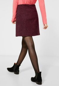 Lila kjol med ett strukturerat mönster, svarta strumpbyxor och svarta ankelstövlar. Kjolen går ovanför knäet och är åtsittande vid midjan.