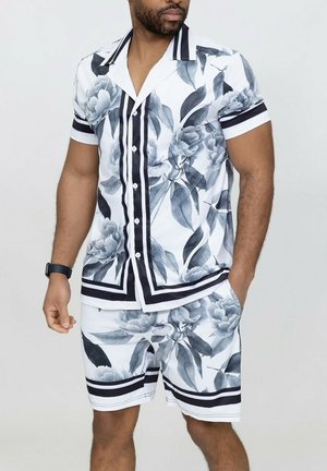 Chemise à manches courtes et short assorti en blanc, noir et gris. Présente un imprimé floral audacieux avec des accents rayés et des boutons.