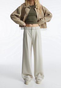 Beige cropped jack, olijfgroen aansluitend top, crèmekleurige comfortabel broek met wijde pijpen, gedetailleerde riem, minimalistisch ontwerp, gladde textuur, casual stijl.
