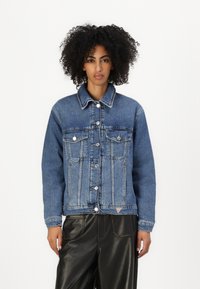 Denim jacket in dark blue with a buttoned front, two chest pockets, and a cropped fit. Features contrasting stitching and a small brand logo.