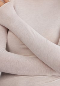 Ljus beige långärmad topp gjord av mjukt, tunt tyg. Har åtsittande ärmar med lätt utsvängning vid manschetterna. Slät textur, minimal formning.