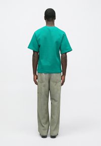 Πράσινη βαμβακερή μπλούζα με χαλαρή εφαρμογή και κοντά μανίκια, σε συνδυασμό με ψηλόμεσο, φαρδύ ανοιχτό γκρι τζιν με ξεθωριασμένο φινίρισμα.