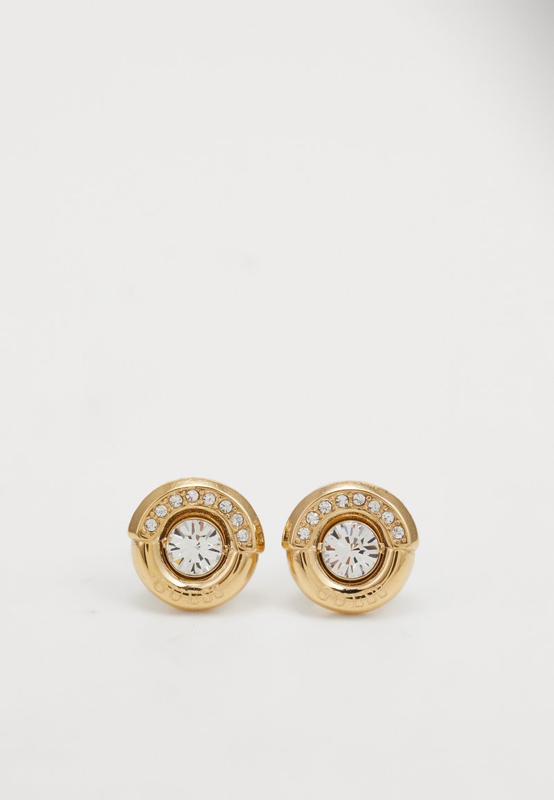 Brincos de stud em tom de ouro com uma pedra clara central rodeada por um design circular com cristais de acento ao longo da borda superior.