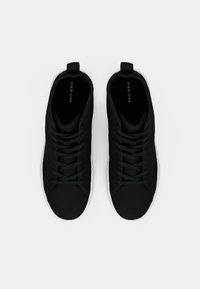 Svarte, uformelle sneakers med et glatt tekstiloverdel, snøring og hvit gummisåle. Har en subtil logo inni skoen.