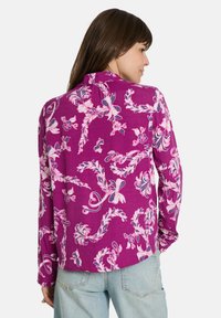 Langarm-Bluse in Lila mit weißen und rosa Blumenmustern, aus weichem Stoff mit lässiger Passform und einem Verschluss am Rücken.
